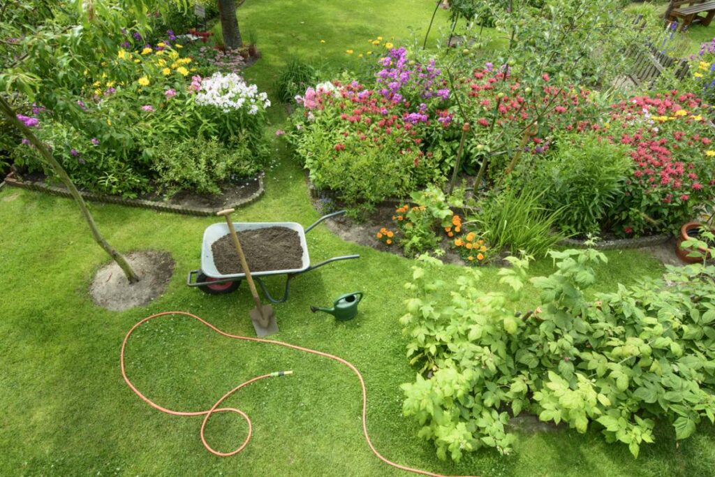 Garden with flowers, wheelbarrow of soil, and gardening tools. A landscaper's paradise.