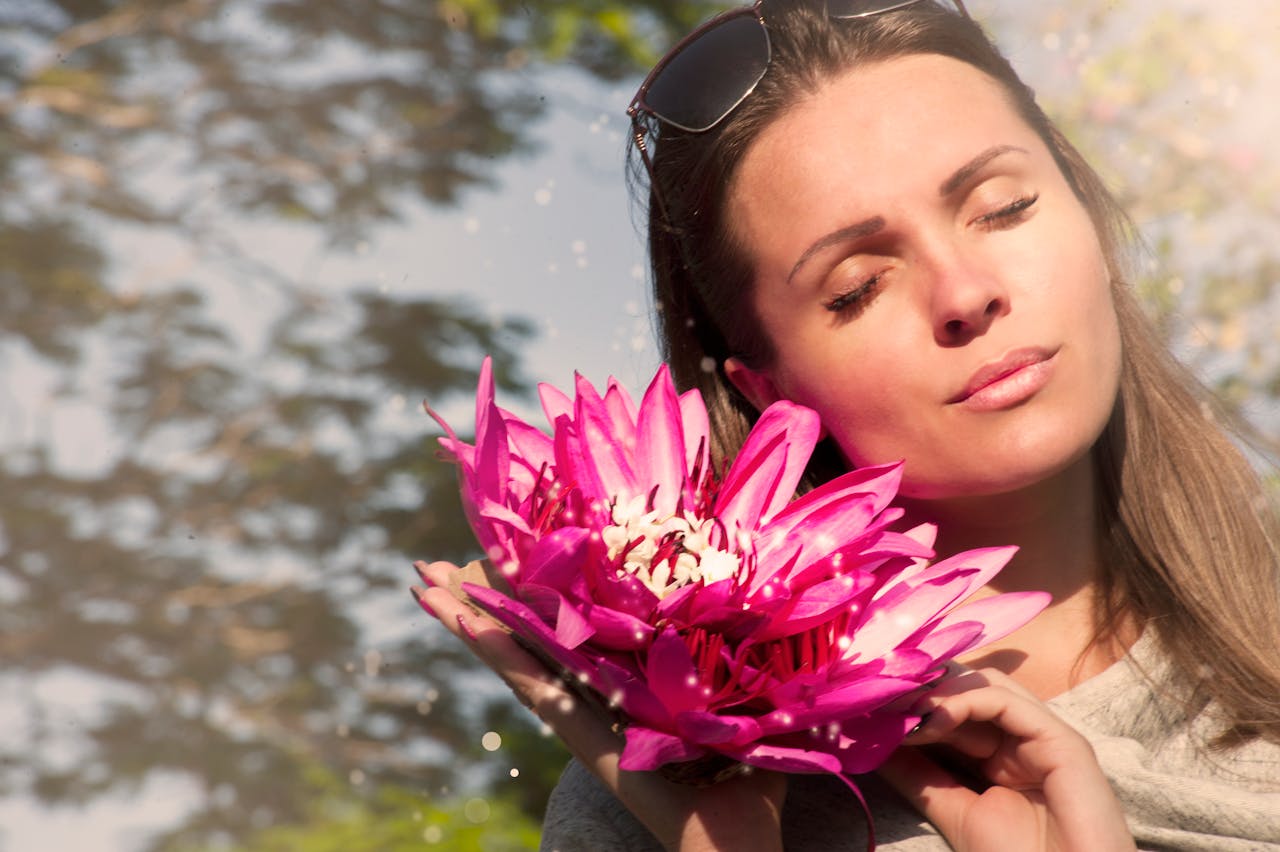 Woman holding a vibrant pink lotus flower, enjoying the sun.