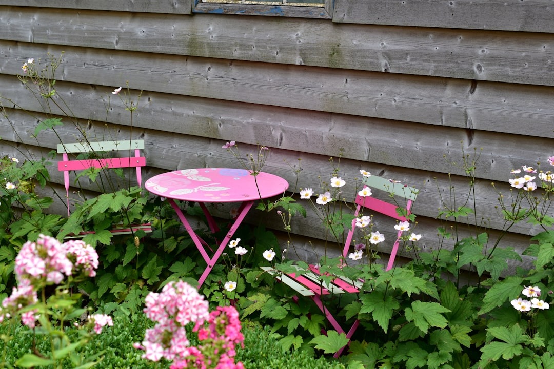 Pink bistro set surrounded by flowers in a backyard garden nook.