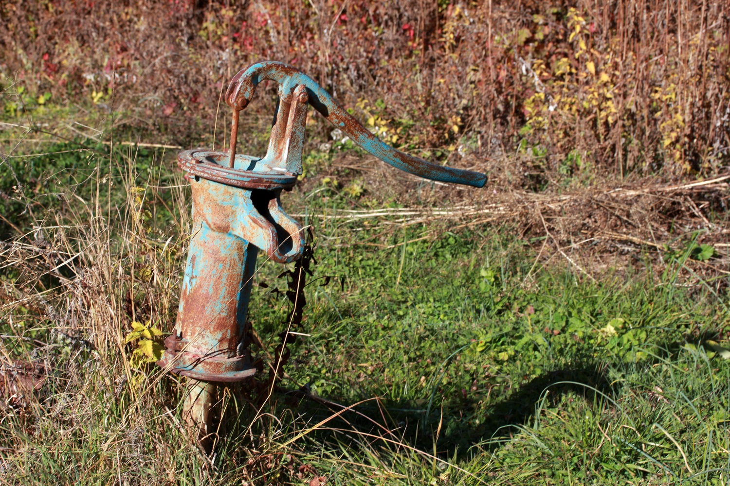 Rusty, vintage hand water pump in a grassy field. Well pump.