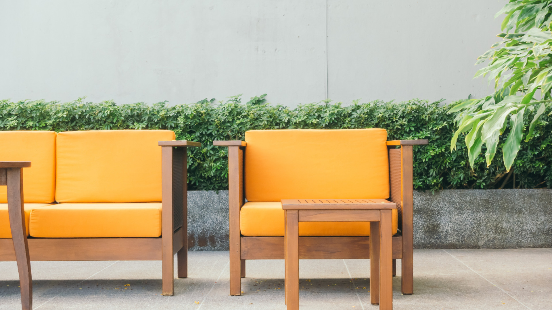 Outdoor seating with orange cushions and wooden frames, plants in background.