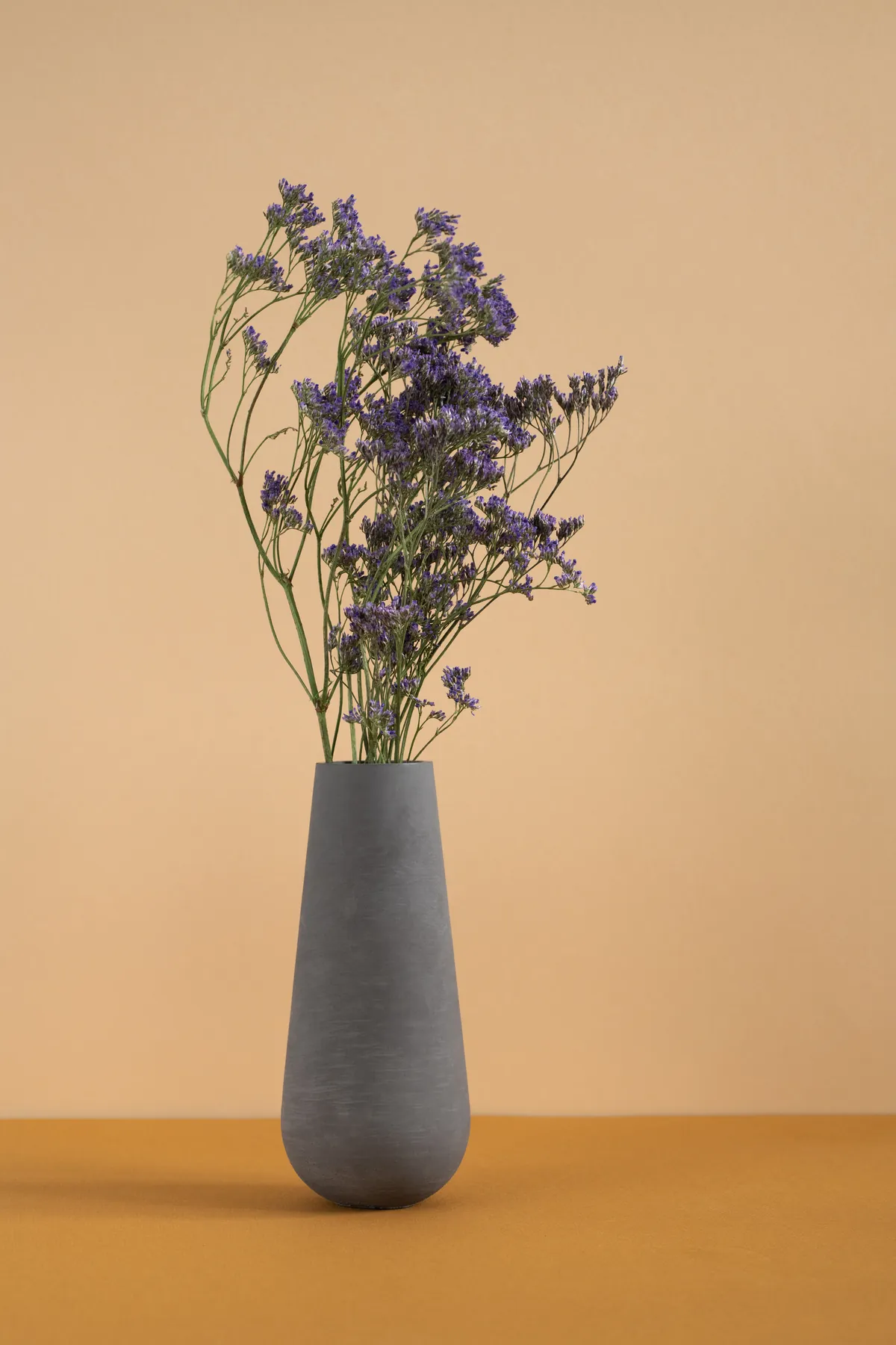 Dried purple flowers in a gray vase against a warm background. Simple floral arrangement.