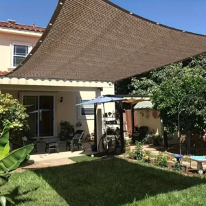 Brown shade sail providing patio cover for an outdoor living space and garden.