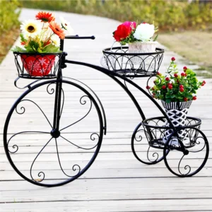 Black metal tricycle planter with colorful flowers in pots on a wooden walkway.