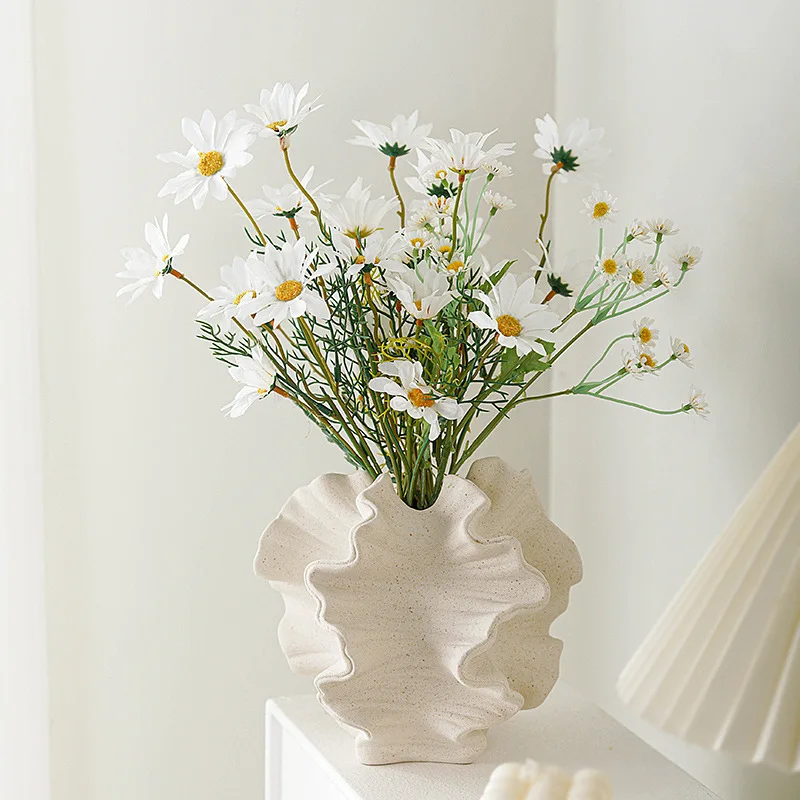 Daisies in a textured, modern vase on a white surface.