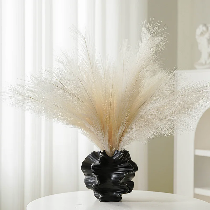 Pampas grass in a black decorative vase on a white table.