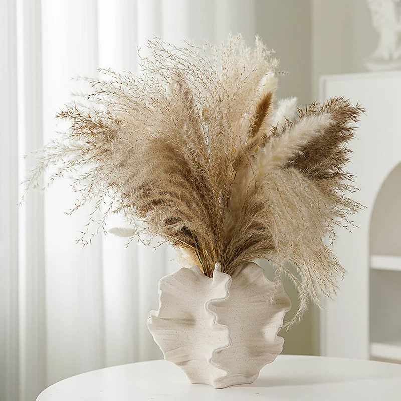 Pampas grass arrangement in a modern, textured vase on a white table.